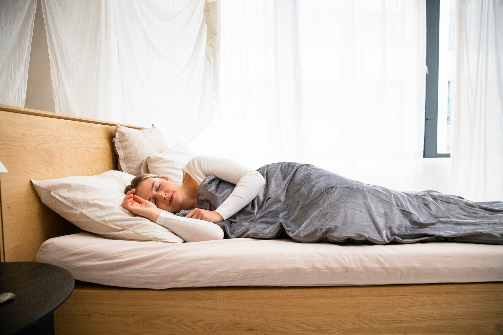 Woman sleeping peacefully on her side in a bright bedroom - side sleeping is the most effective drug-free way to stop snoring