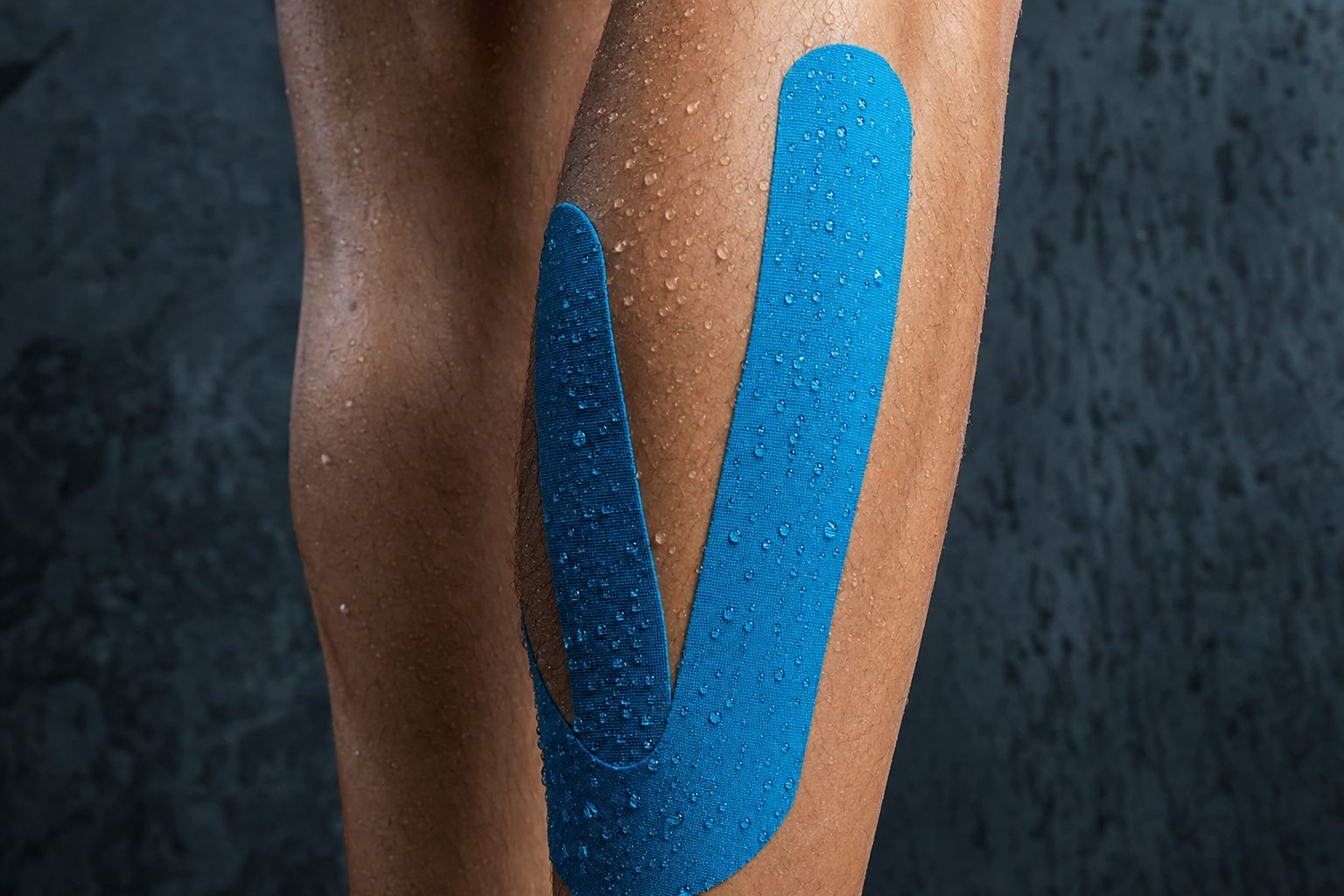 Runner's leg with blue kinesiology tape and water droplets — TapeGeeks waterproof KT tape after shower