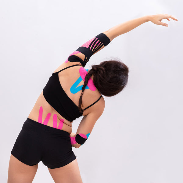 Active woman stretching with pink, blue, and black TapeGeeks kinesiology tape on arm, back, and hip for flexible muscle support.