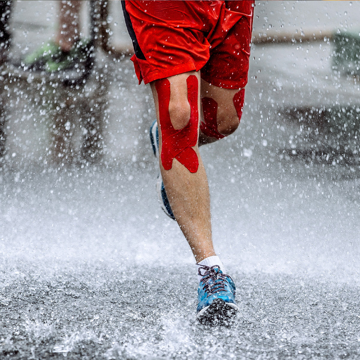 Runner wearing red TapeGeeks kinesiology tape on knees in rain, showing strong, water-resistant muscle and joint support.
