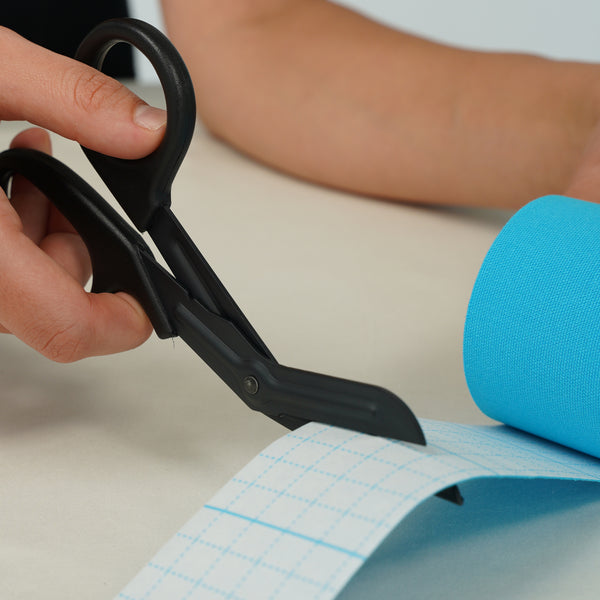 TapeGeeks medical scissors cutting a strip of kinesiology tape, showing safe blunted tips and smooth cutting for runners applying tape.