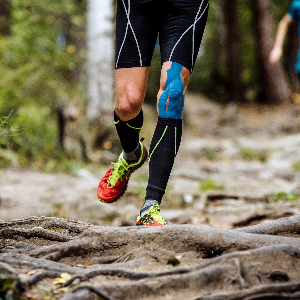 Trail runner wearing blue kinesiology tape on the knee for added stability and injury prevention during outdoor running.
